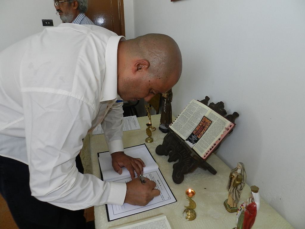 Irmão assinando o livro da fraternidade diante da cruz de São Damião